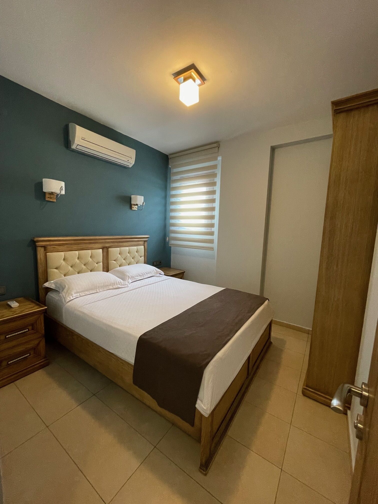 Un dormitorio con una cama grande, un cabecero de madera, una mesita de noche, un armario y una lámpara en el techo.