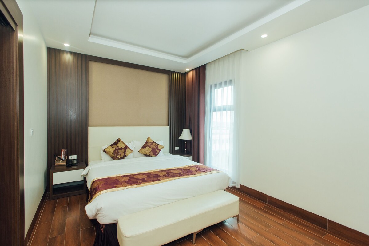A hotel room with a large bed, a bedside table, a lamp, and a window with curtains.