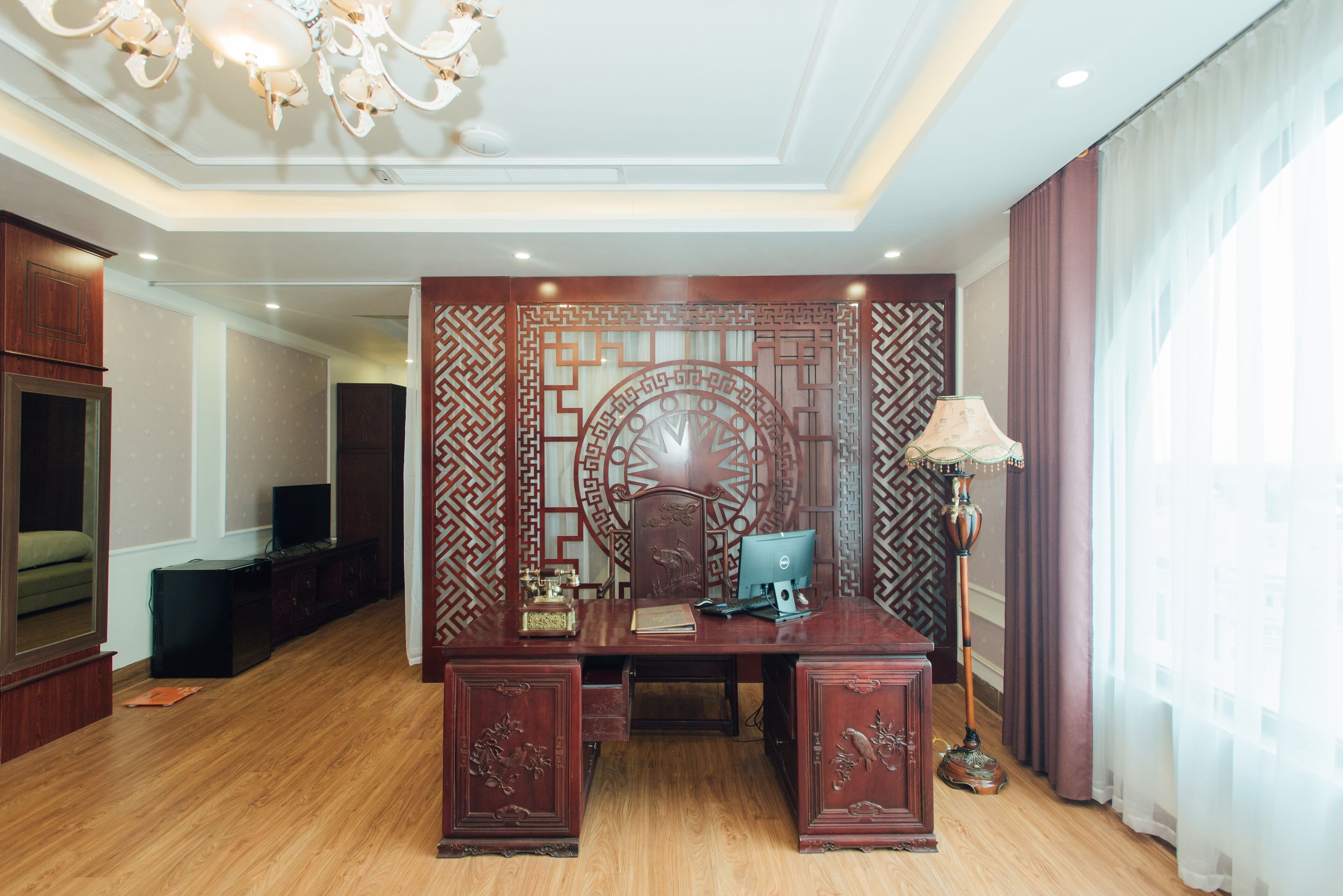 A room with a wooden desk, a computer, a lamp, and a decorative wall panel.