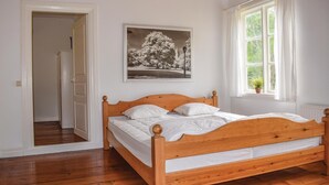 A bedroom with a wooden bed, white walls, a framed black and white photograph, and a window with a view of greenery.