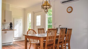 A dining area with a wooden table and chairs, a hanging light fixture, and a clock on the wall.