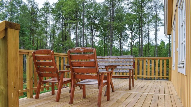 A wooden deck with two wooden chairs and a table, surrounded by a wooden railing, overlooking a forest.