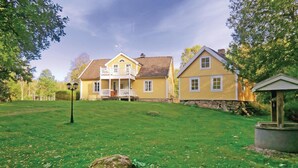 A two-story yellow house with a balcony, a stone wall, and a small gazebo in the foreground.