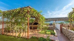 Un espacio exterior cubierto con un horno de piedra, una pérgola con plantas trepadoras y un muro de piedra.