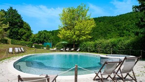 A swimming pool with lounge chairs and a hammock, surrounded by lush greenery and hills.
