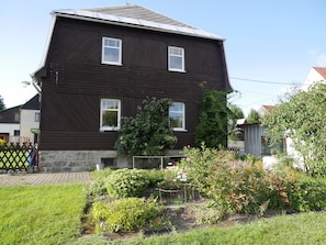 A two-story house with a dark brown exterior, multiple windows, and a garden with various plants and flowers.