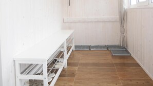 Una stanza con pareti in legno, una panca bianca, un portascarpe e una finestra.