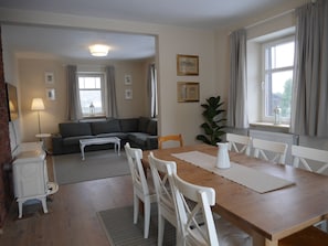A living room with a sofa, a dining table with chairs, a lamp, and a radiator.