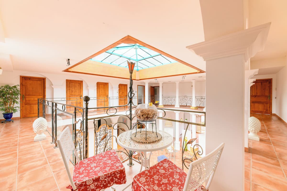 Un intérieur spacieux avec un plafond haut, une verrière centrale et un coin repas avec des tables et des chaises rondes.