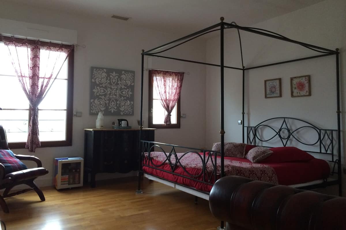 Une chambre à coucher avec un lit à baldaquin, un plancher en bois, un bureau avec une chaise et deux fenêtres avec des rideaux.