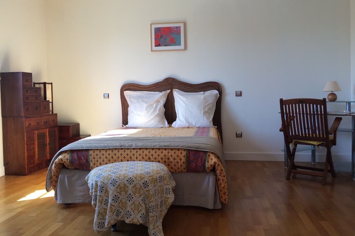 Une chambre à coucher avec un lit en bois, une chaise, une commode et un tableau encadré au mur.