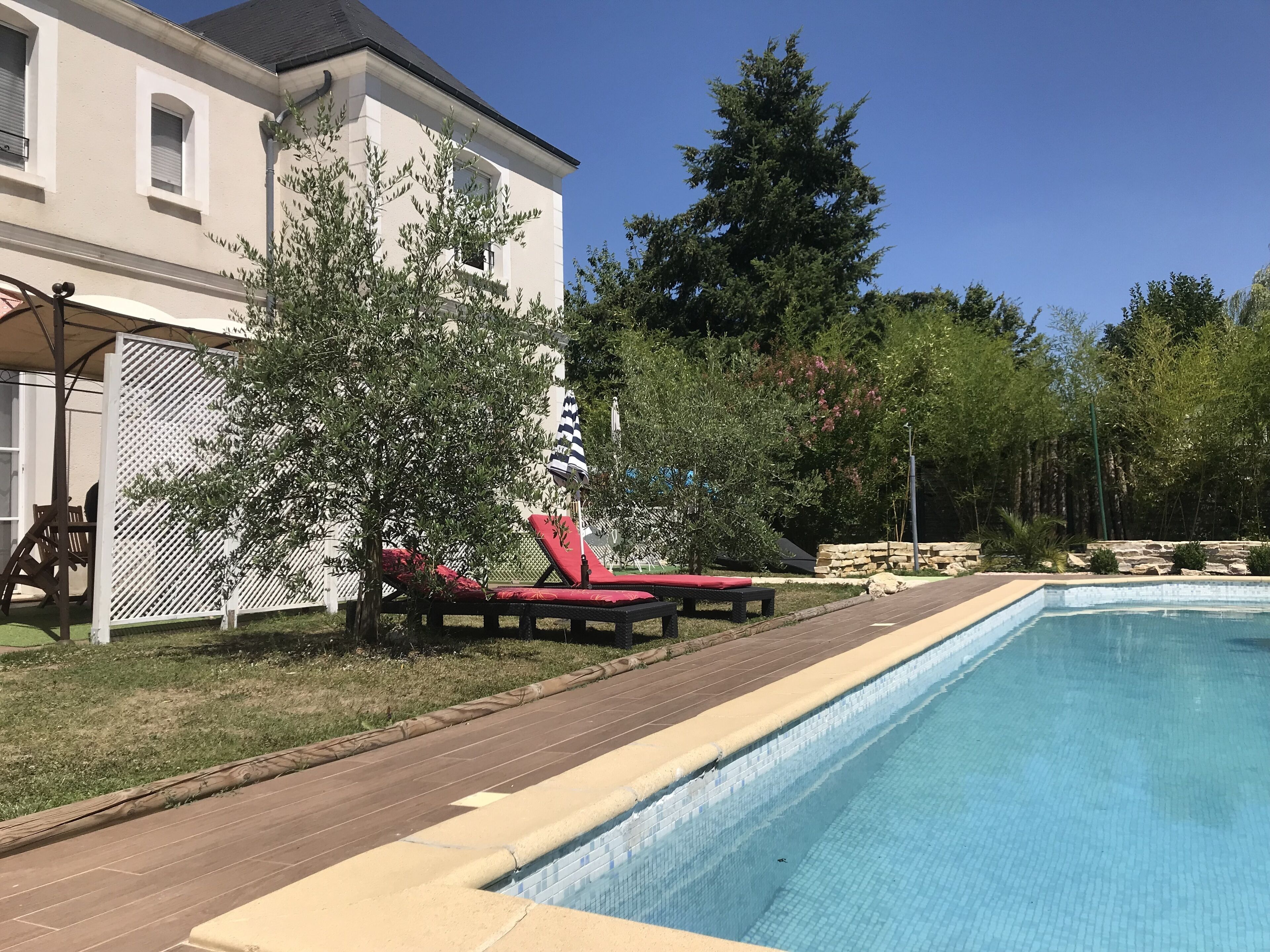 Una piscina con sillas de descanso, un porche cubierto y una casa grande de fachada blanca.