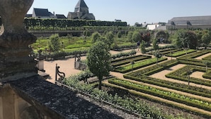 Un jardin à la française, avec des haies aux formes géométriques, et un bâtiment imposant, doté d’un toit en pente, qui se détache sur le fond.
