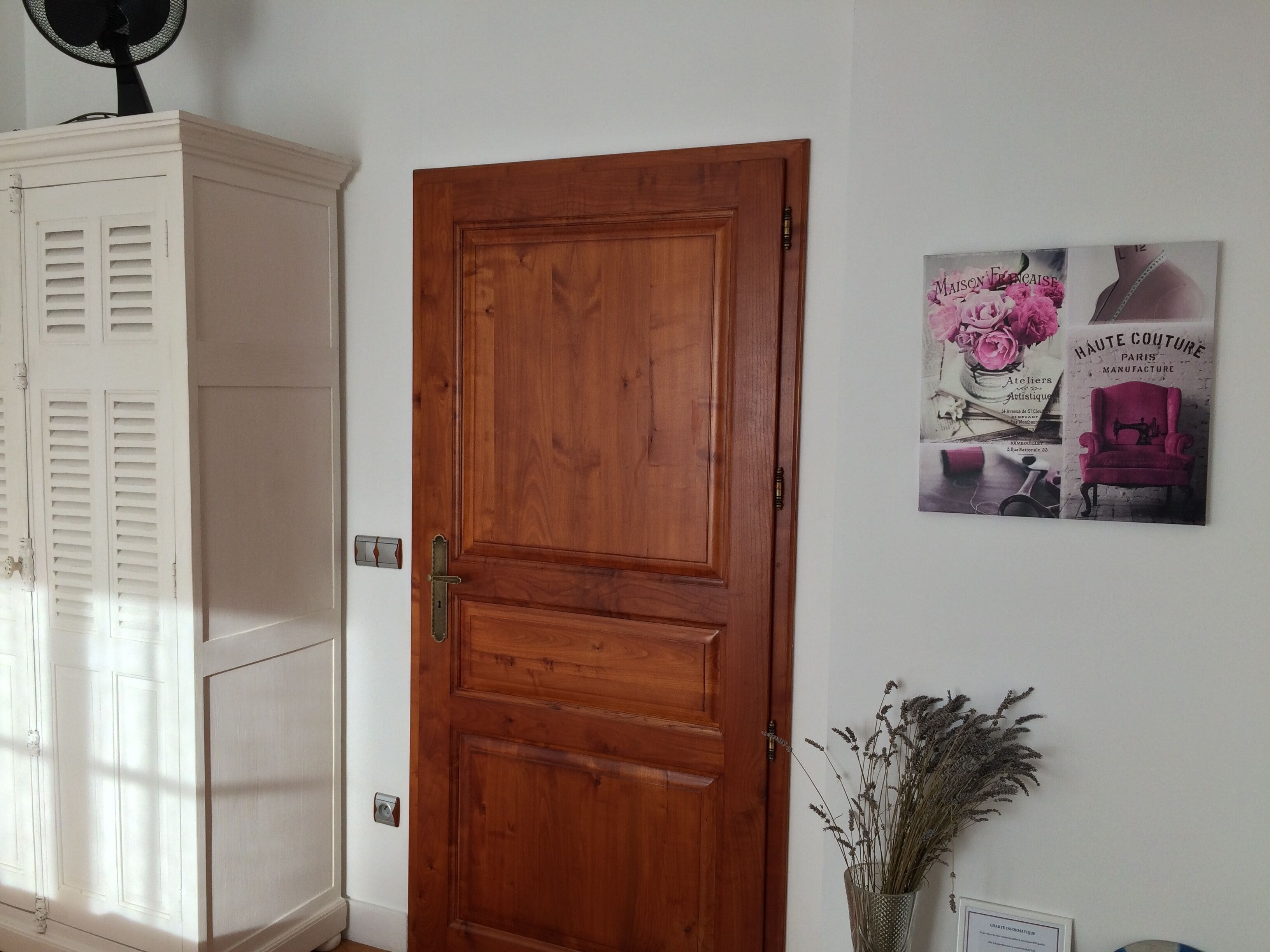 A wooden door with a white cabinet to the left and a poster on the wall.