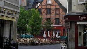 Un espace café en plein air, avec des tables et des chaises, entouré de bâtiments à l’architecture traditionnelle.