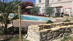 Un espace piscine agrémenté de chaises longues et de parasols, entouré d’un mur de pierre et de verdure.