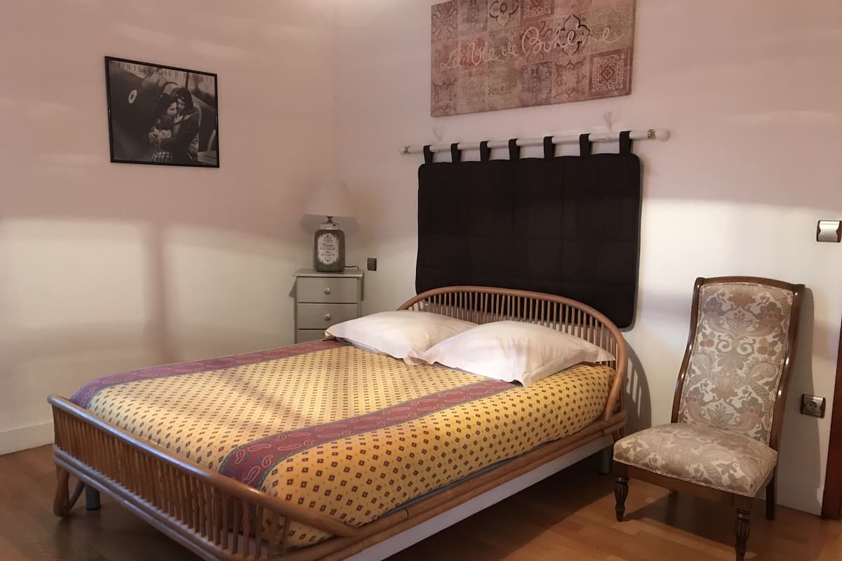 Une chambre à coucher avec un lit en bois, une chaise, une table de chevet, une lampe et un élément décoratif mural.