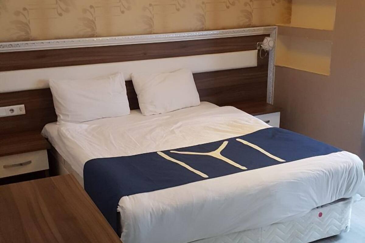 Een slaapkamer met een bed, een houten nachtkastje, een wandlamp en behang met een patroon.