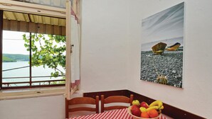 A dining area with a checkered tablecloth, a bowl of fruit, and a painting of boats on a rocky shore. - 2 bedroom cozy home in Trget (Trget)