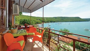 A balcony with orange chairs and a table, overlooking a lake with boats and a green hillside. - 2 bedroom cozy home in Trget (Trget)