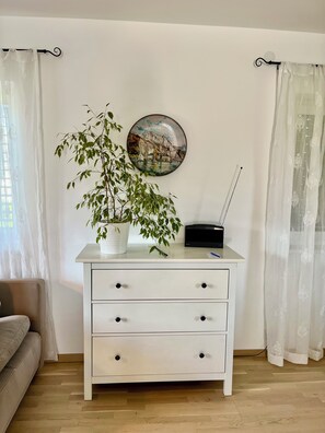Ein weißer Kommode mit Schubladen, ein Blumentopf, ein an der Wand befestigtes Radio und ein gerahmtes Bild.