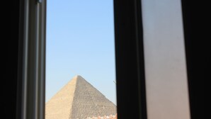 Vista de una pirámide a través de una ventana, con cielo despejado al fondo.