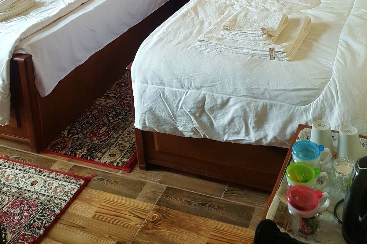 A hotel room with two single beds, a wooden headboard, a nightstand, a small table with a teapot, cups, and a kettle.