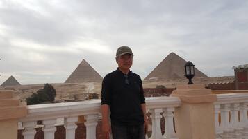 A man standing in front of the Great Pyramids of Giza with a view of the pyramids and a lamp post in the foreground.
