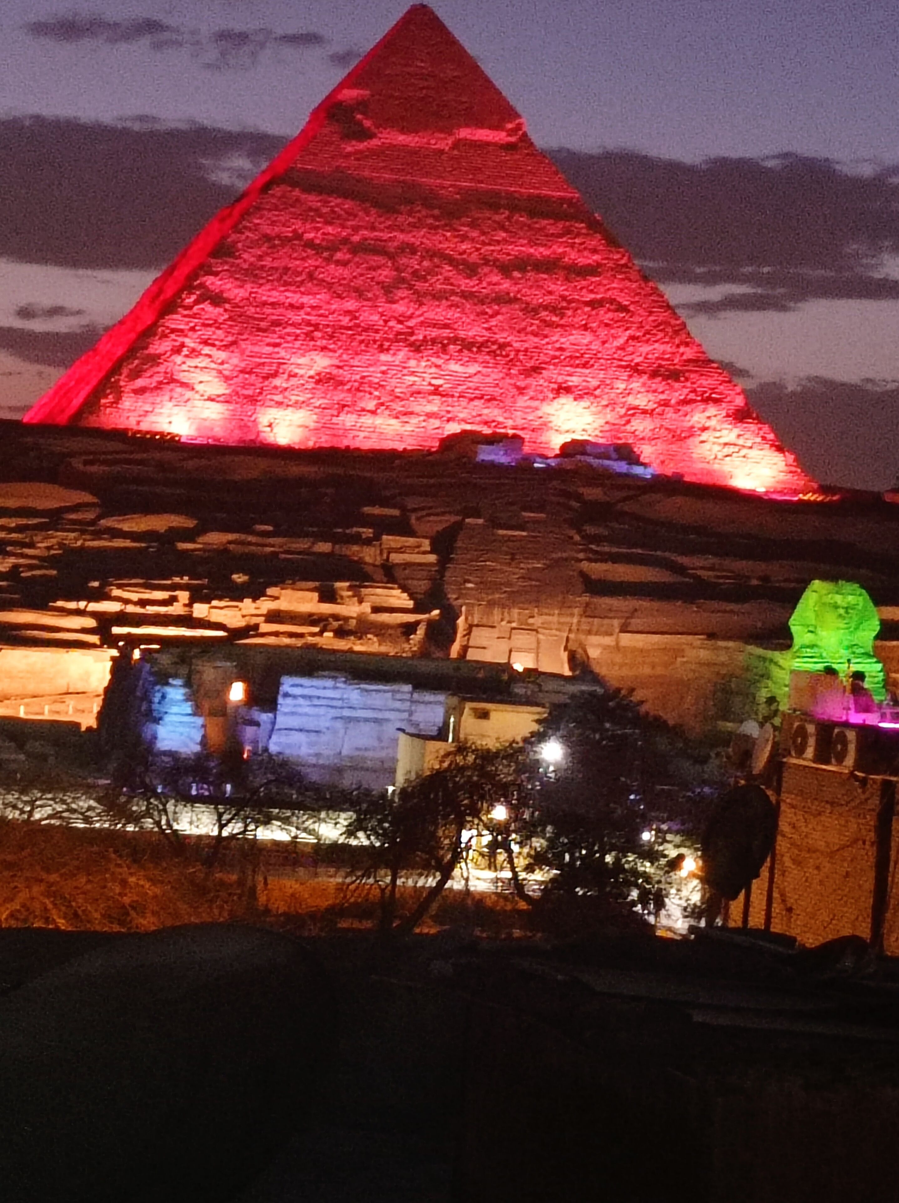 A pyramid-shaped building with a red-lit top, surrounded by stone structures and trees.