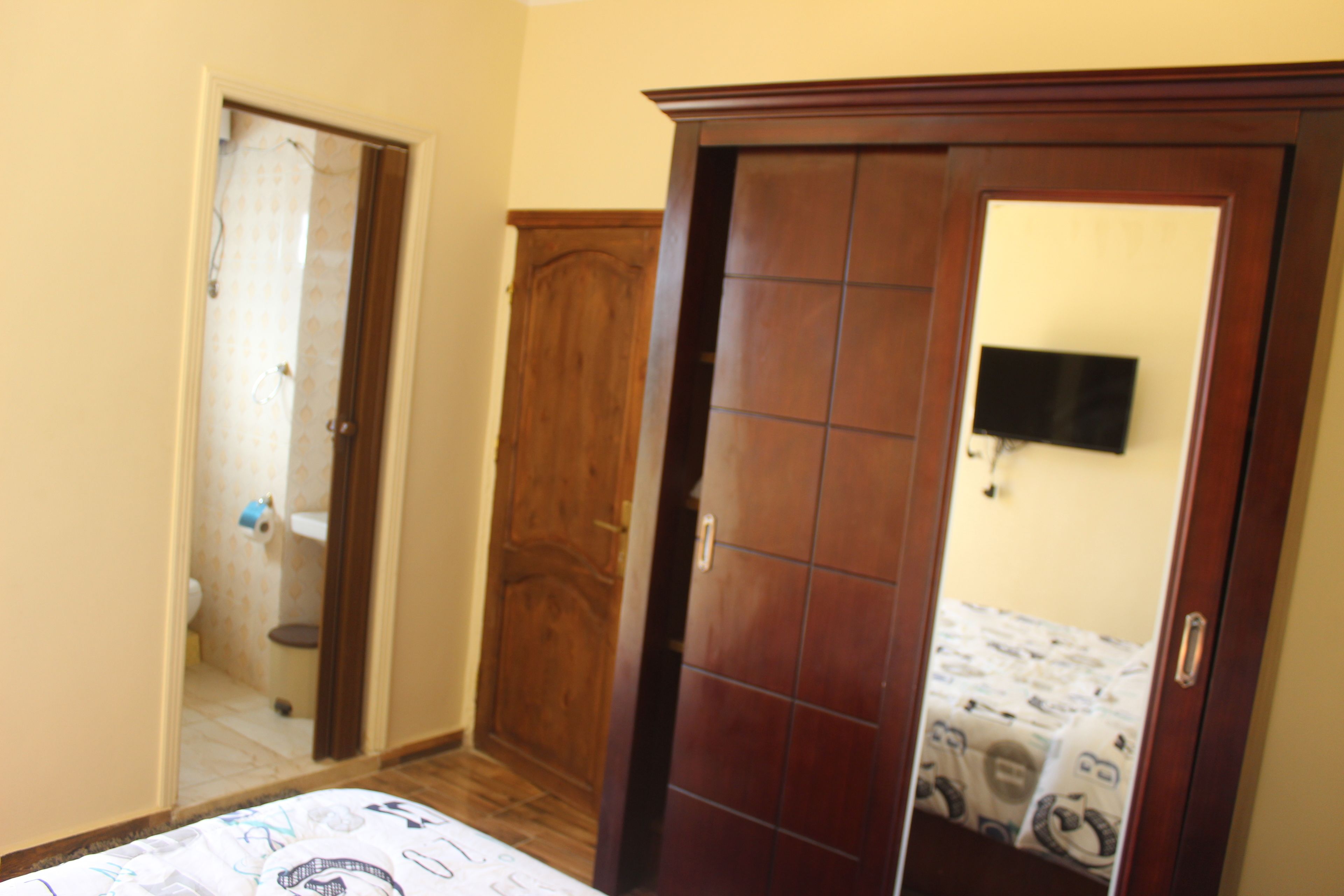 Un dormitorio con un armario de madera, una cama con ropa de cama estampada y un televisor montado en la pared.