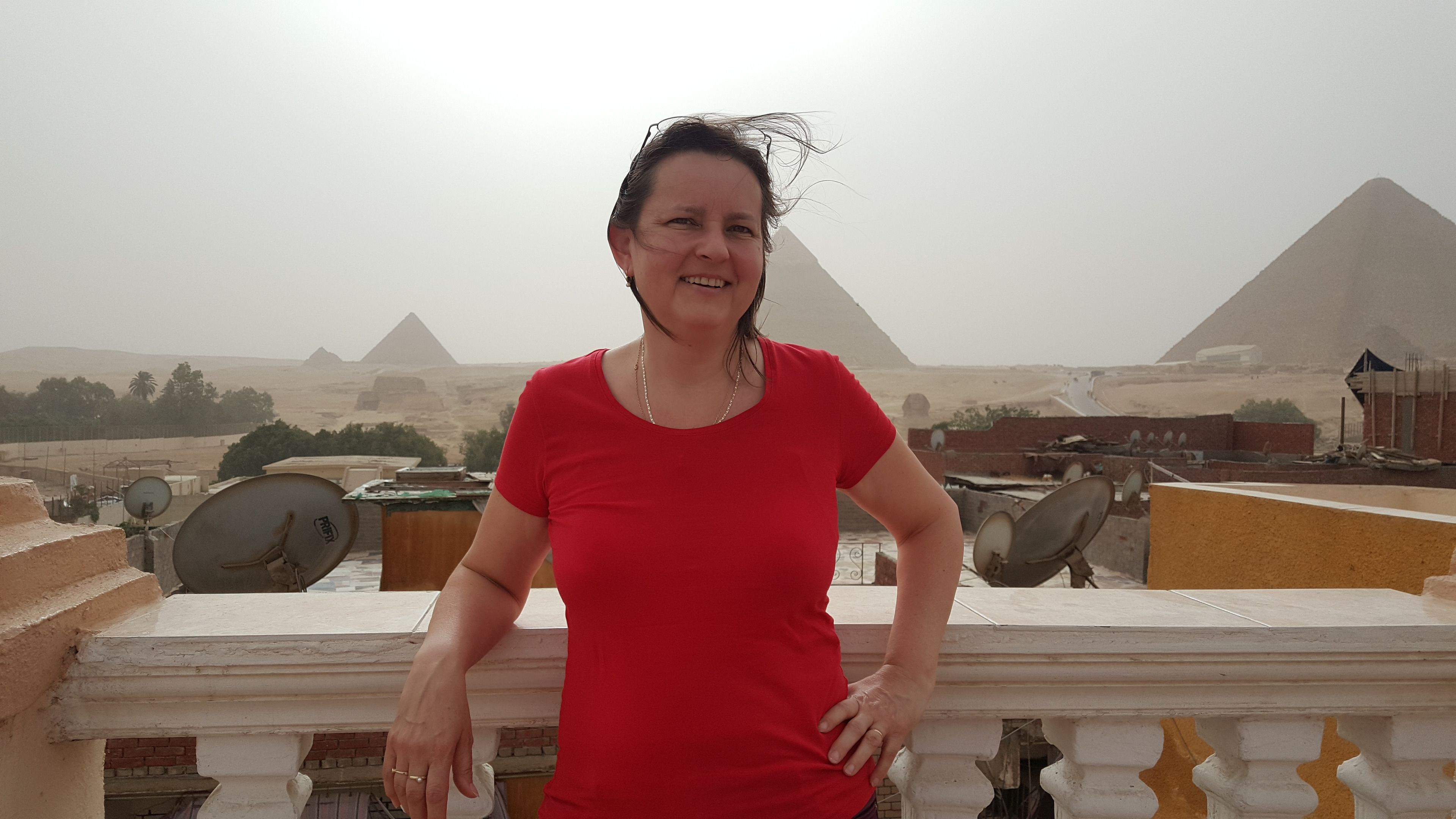 A person standing on a balcony with a view of pyramids in the background.
