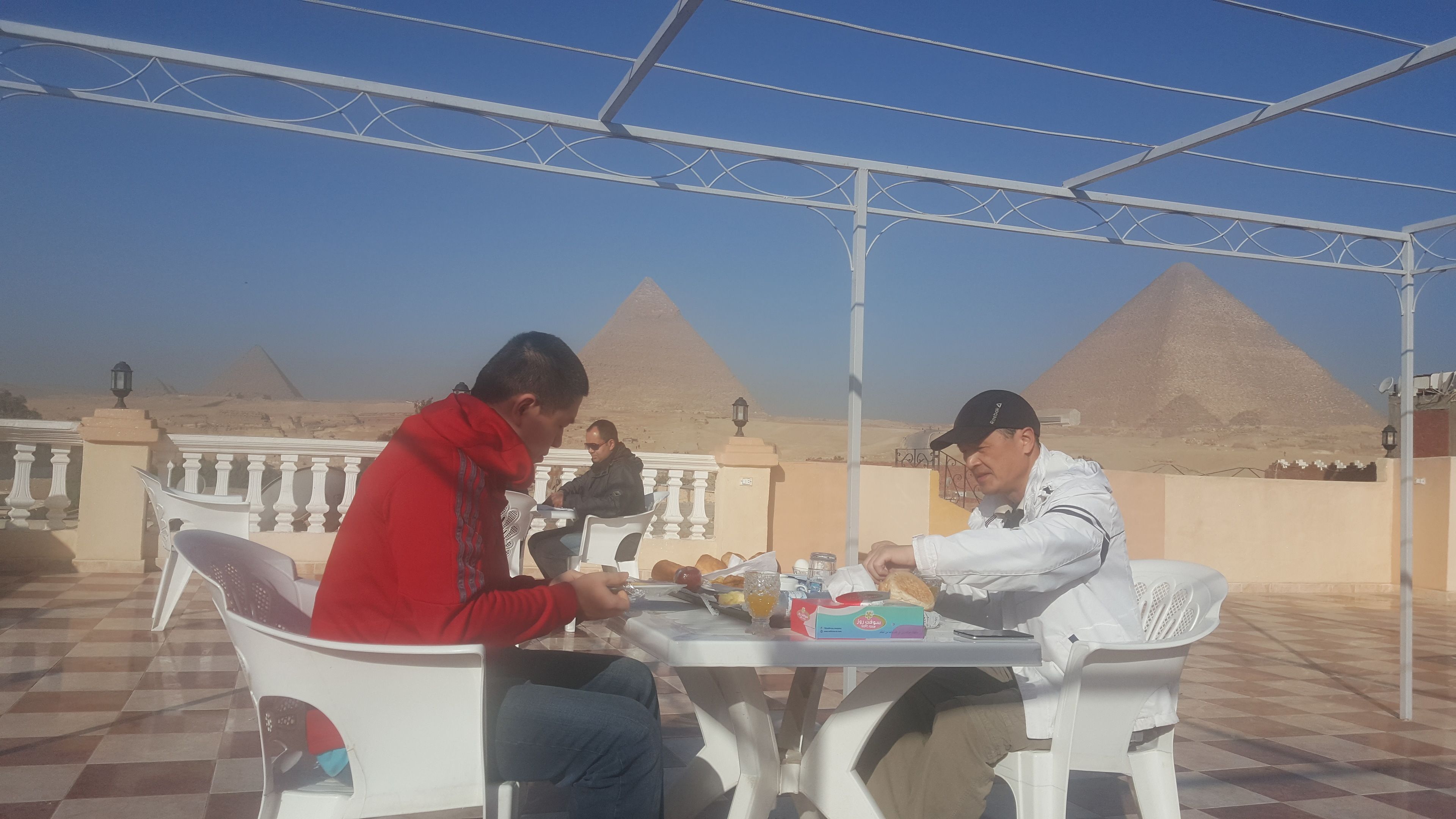 A terrace with a view of pyramids, featuring outdoor seating and a table with food and drinks.