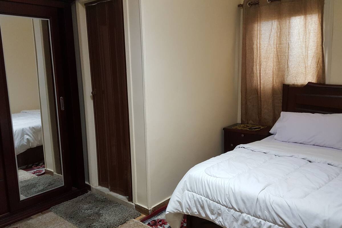A bedroom with a bed, a nightstand, a mirror, and a wardrobe.