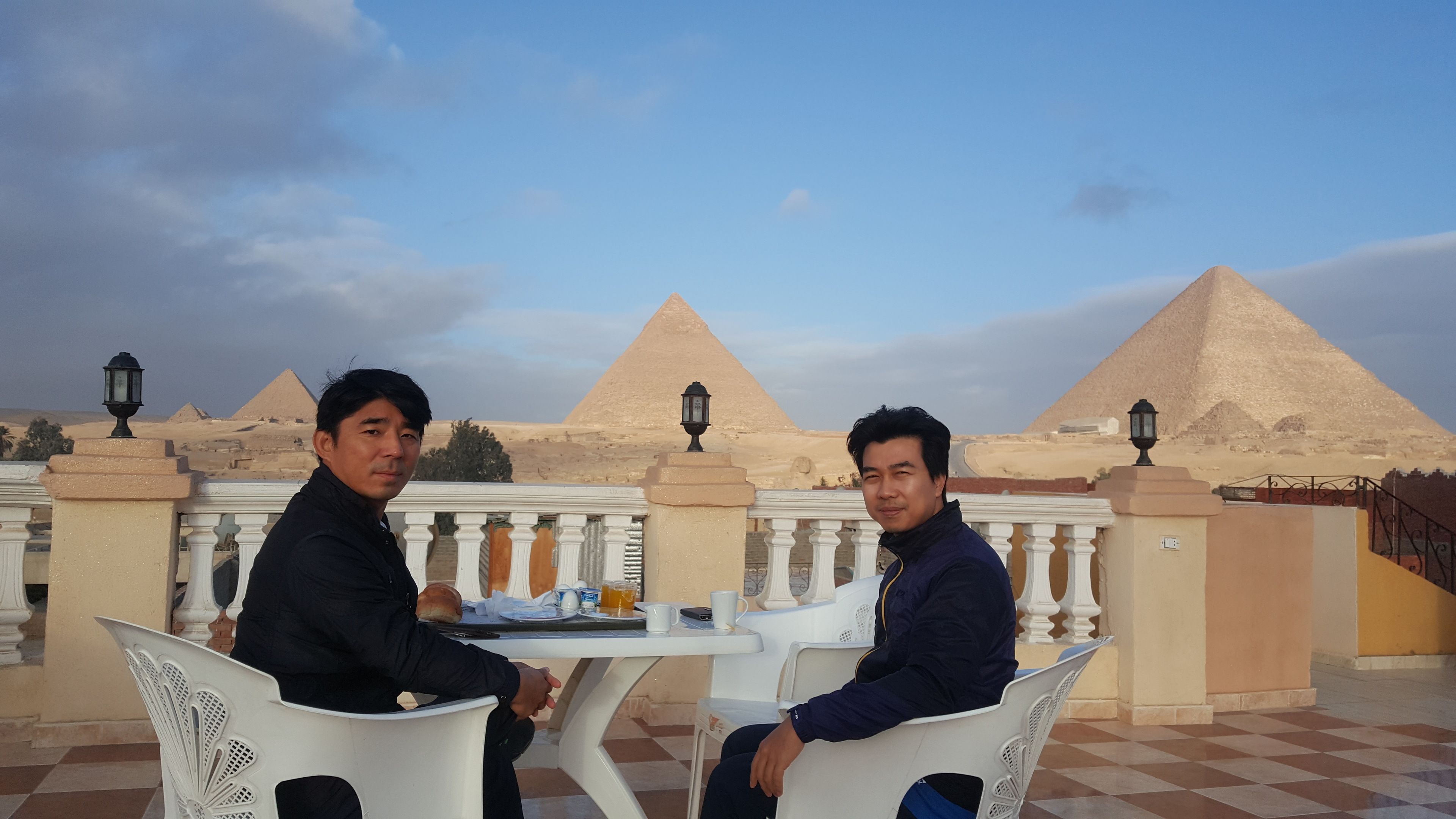 Two men seated at a table with a view of the pyramids in the background.