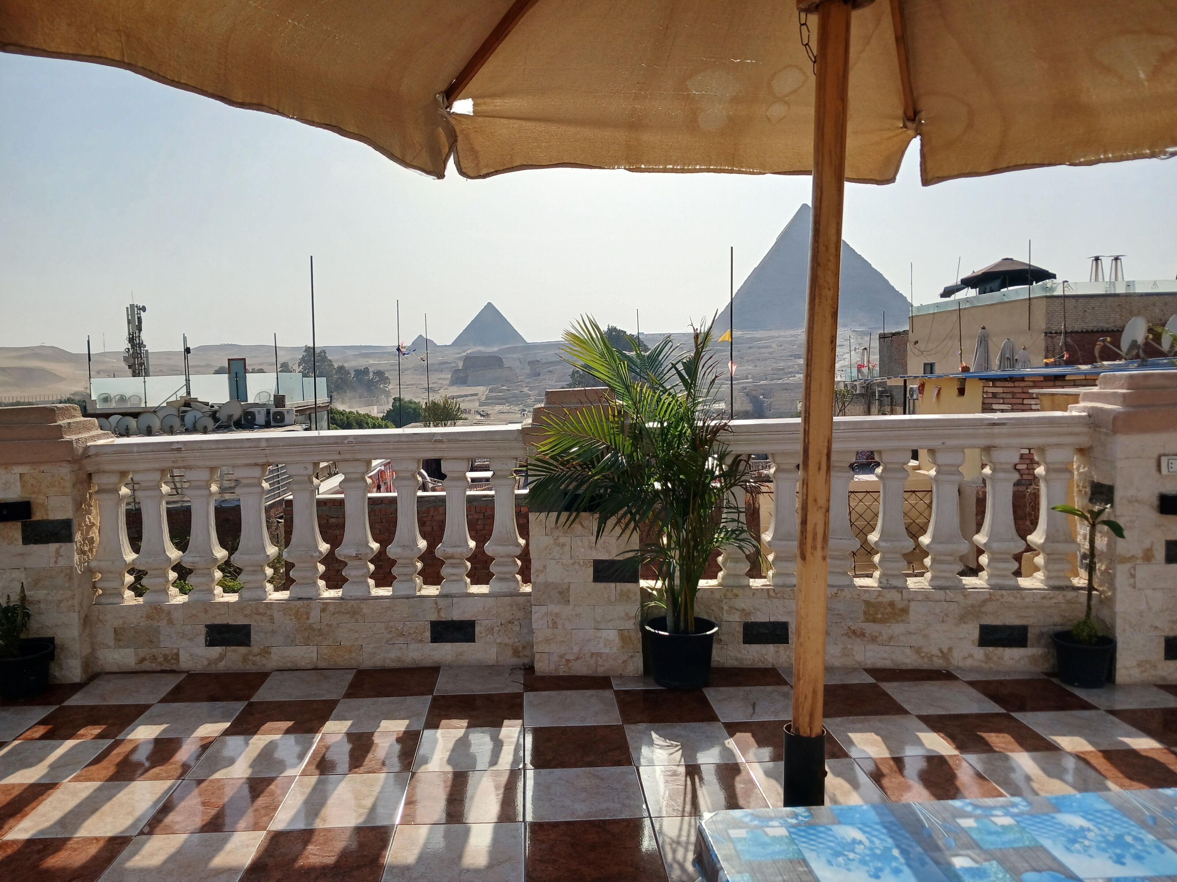 A terrace with a checkered floor, a potted plant, and a view of pyramids in the distance.