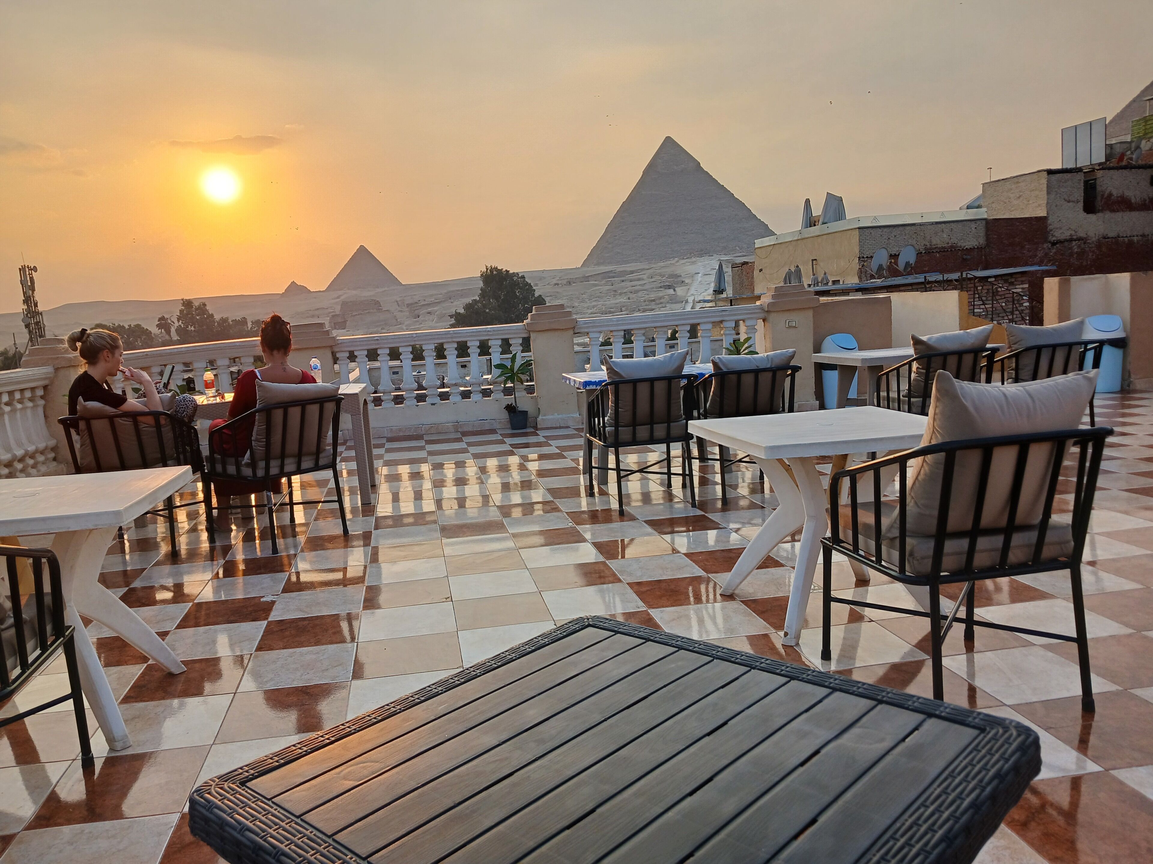 A terrace with checkered flooring, outdoor seating, and a view of the pyramids.