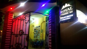 La entrada a Royal Pyramids Inn, con un letrero, un portón metálico decorativo y algunas sillas de plástico afuera.
