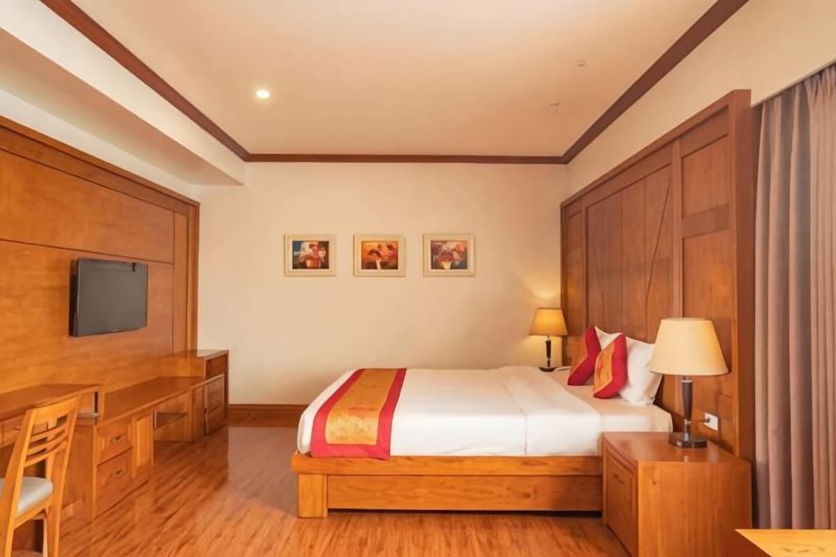 Een hotelkamer met een houten bed, nachtkastje, lamp, bureau, stoel en een flatscreen televisie.