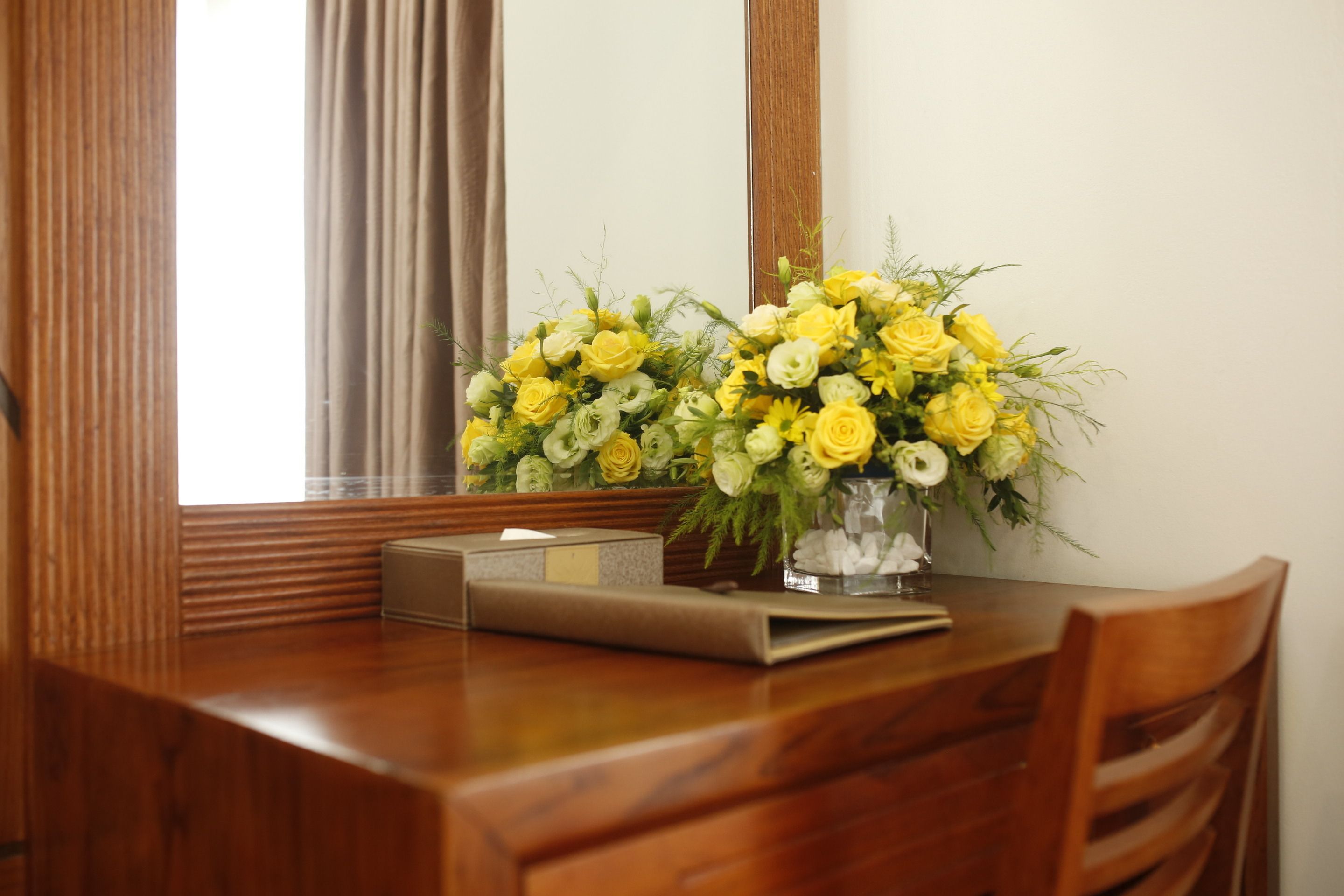 A wooden table with a vase of yellow flowers and a tissue box.