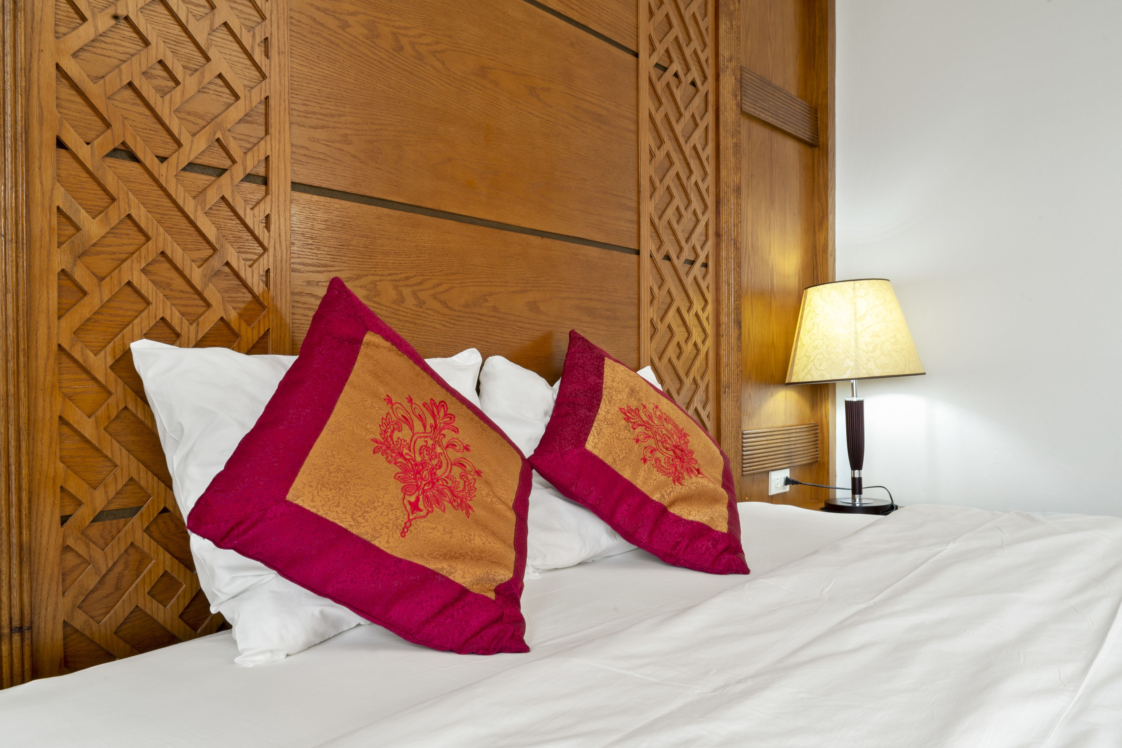A neatly made bed with white sheets and two decorative pillows with a geometric pattern.