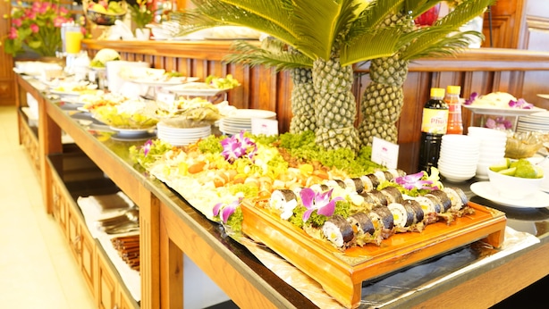 A buffet with various dishes, including sushi, arranged on a wooden table with a large pineapple centerpiece.