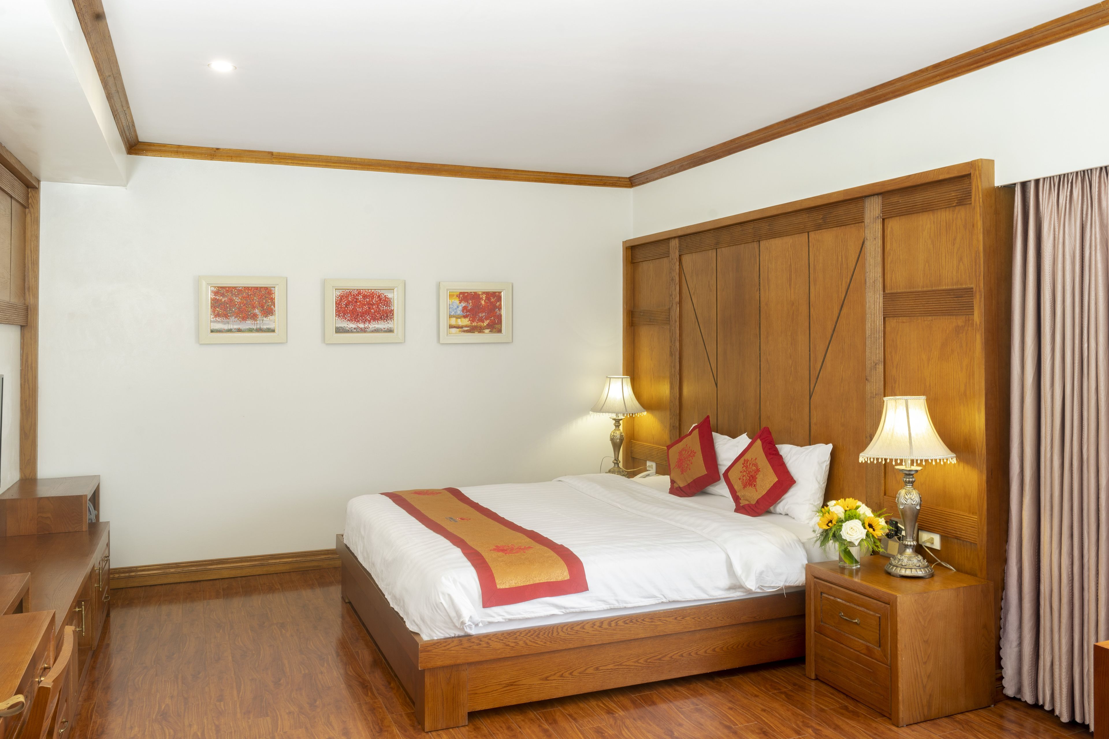 Une chambre d’hôtel bien rangée, avec un lit en bois, des tables de chevet dotées de lampes et des œuvres d’art encadrées accrochées au mur.