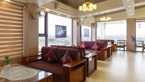 A spacious living area with a large window offering a city view, a comfortable seating area with a sofa and chairs, and a chandelier.