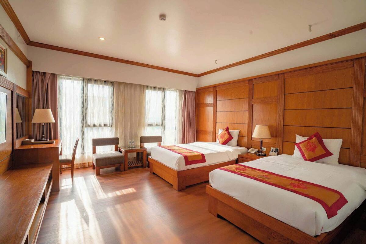 A hotel room with two beds, a desk, a chair, and a window with curtains.