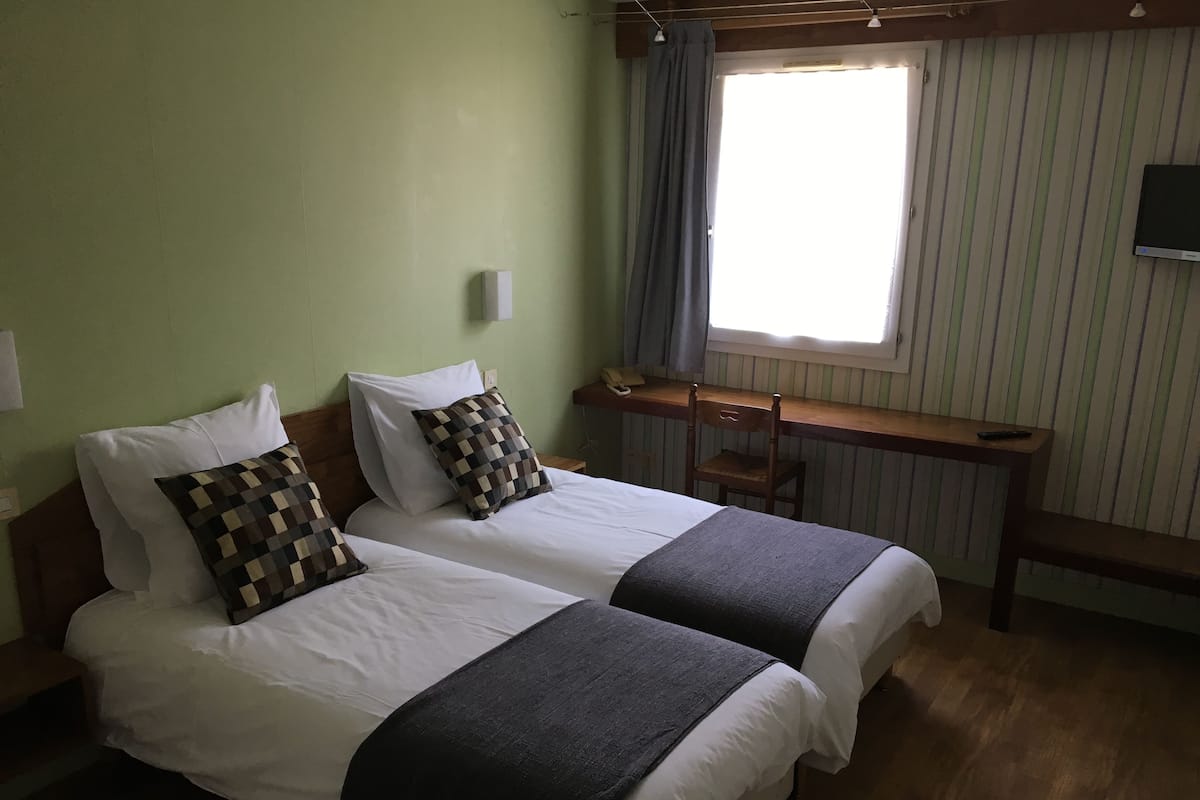 Une chambre avec deux lits, un bureau et une fenêtre avec des rideaux.