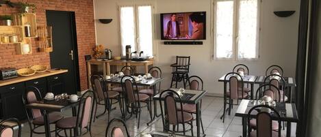 A dining area with multiple tables and chairs, a brick wall, a television, and a kitchen area with shelves and utensils.