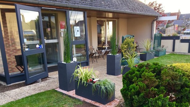 A modern building with large glass doors, outdoor seating, and potted plants. - Hôtel Le Dauphin (Saint-Denis-de-l'Hôtel)