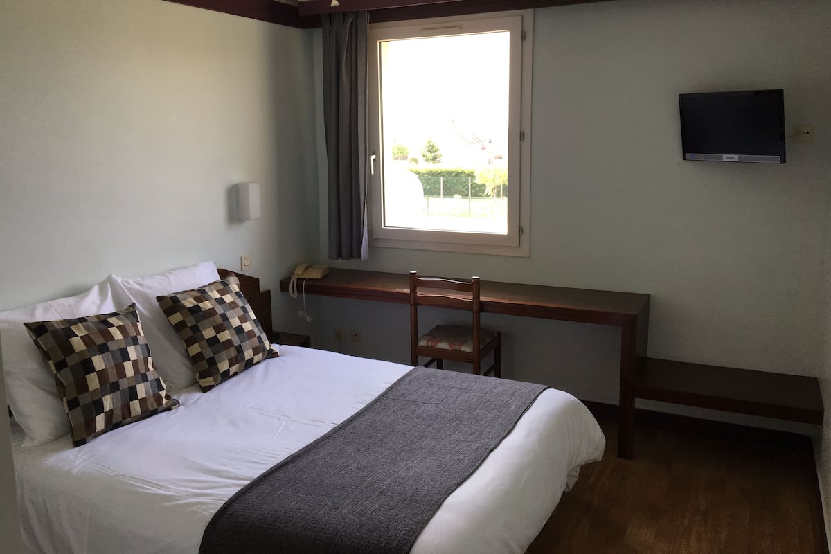 Une chambre d’hôtel équipée d’un lit, d’un bureau, d’une chaise, d’une télévision et d’une fenêtre avec des rideaux.