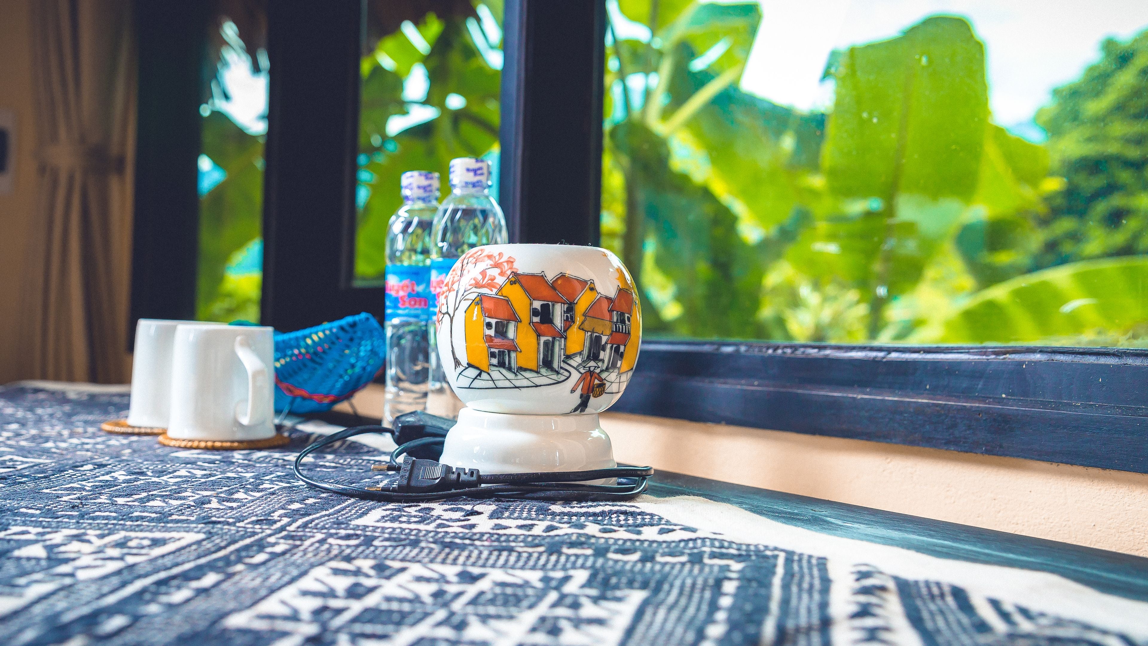 Una habitación con un tapete estampado, una taza de cerámica, un adorno azul y una botella de agua sobre un alféizar.