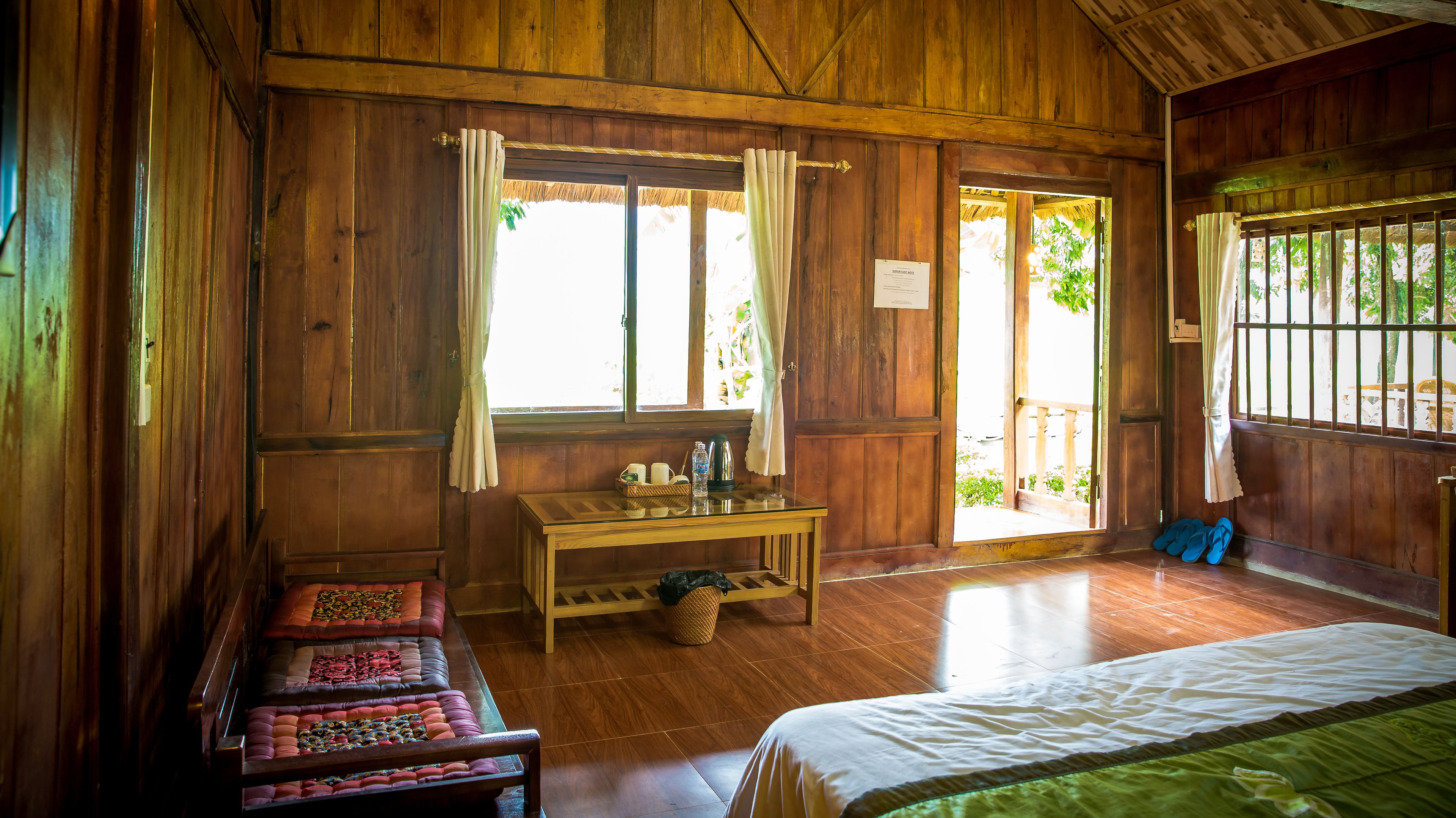 A wooden room with a bed, a table with items, a bench, and a door leading outside.
